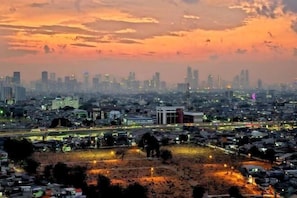 A cityscape at dusk with a prominent building in the foreground and a dense urban area in the background.