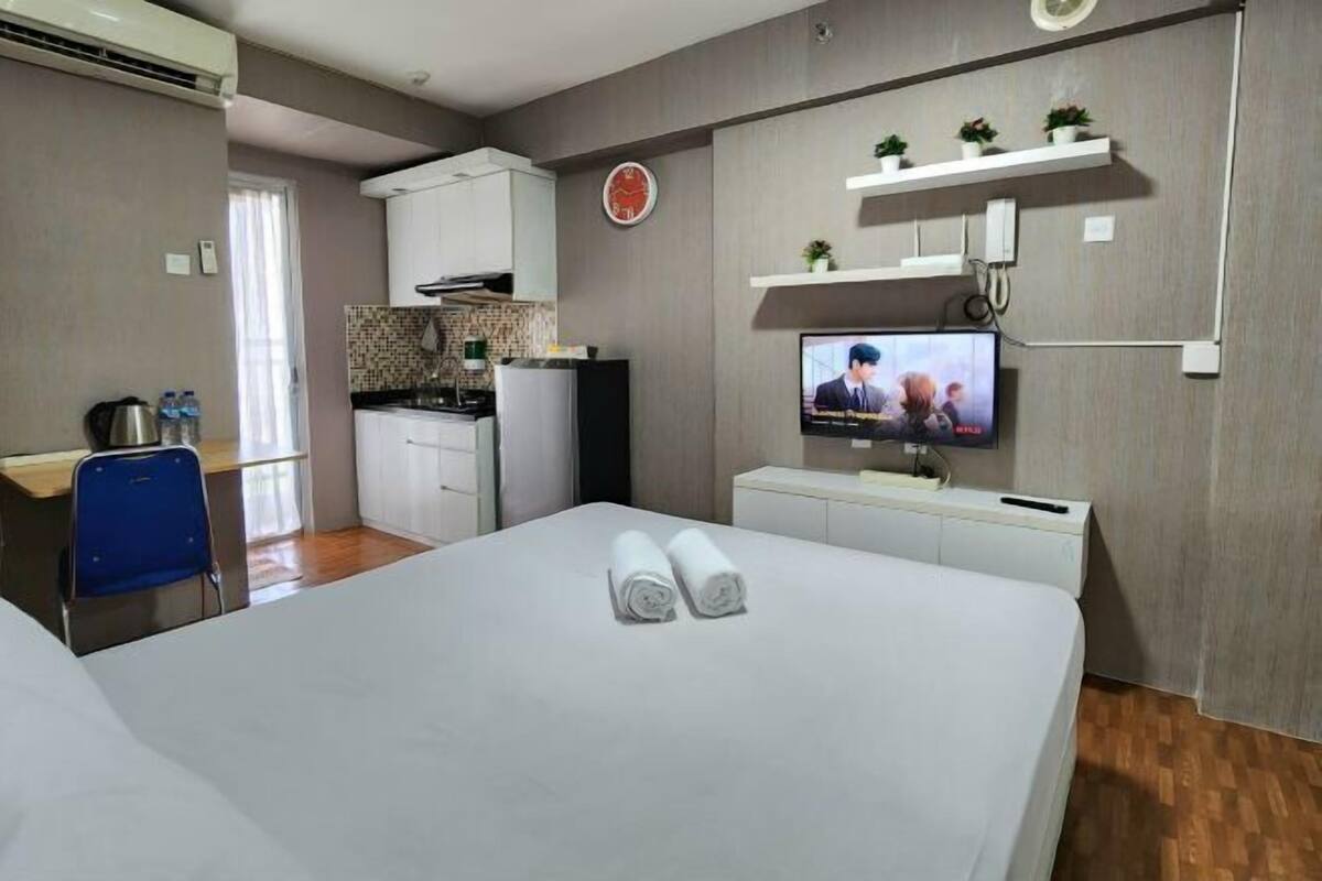 A hotel room with a bed, a desk with a chair, a TV, and a kitchenette.