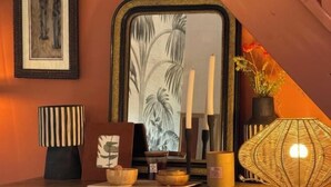 Ein Zimmer mit einem Spiegel, einer gestreiften Lampe, einer Vase mit Blumen und einer dekorativen Schale auf einem Holztisch.