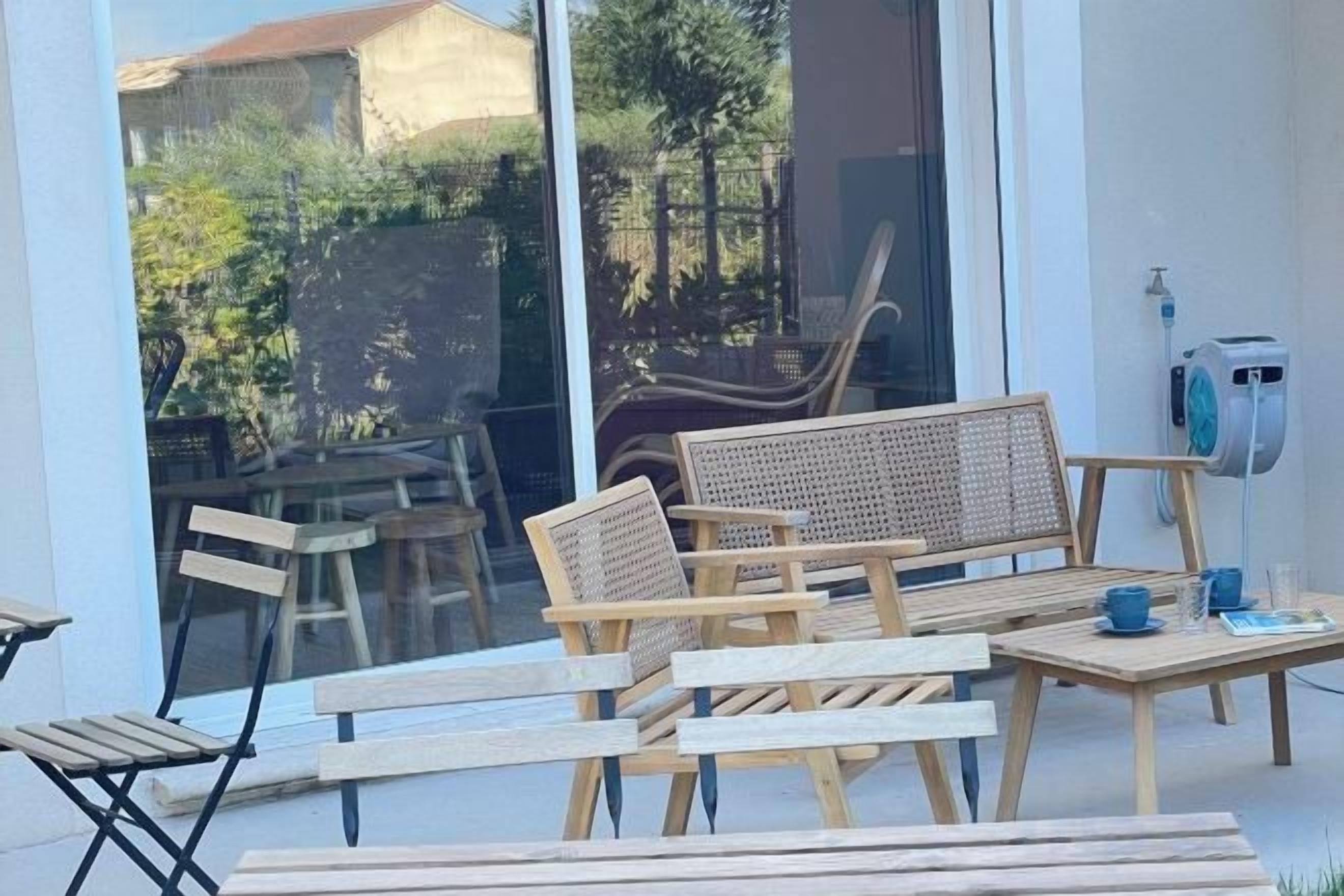 A patio with wooden furniture, including a sofa and chairs, and a table with cups and a book.