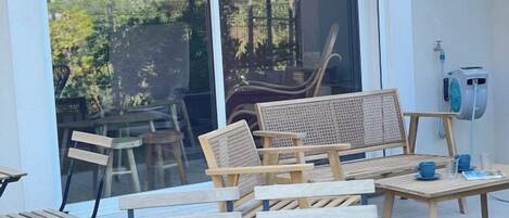 Un patio con mobiliario de madera, incluyendo un sofá, sillas y una mesa con tazas y un libro.