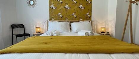 A hotel room with a large bed, two bedside tables with lamps, a black chair, a wooden easel, and a wall with a patterned design.