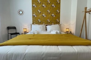 Une chambre d’hôtel avec un grand lit, deux tables de chevet avec des lampes, une chaise noire, un chevalet en bois et un mur orné d’un motif décoratif.