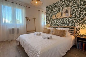 A neatly made bed with rolled towels, a wooden headboard, and a wall with a leaf pattern. - Houses Le Clos Du Moulin (Entraigues-sur-la-Sorgue)