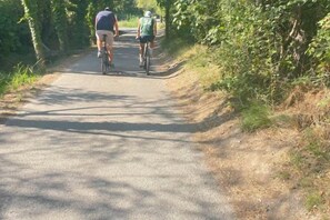 Deux personnes font du vélo sur une piste asphaltée, entourée de verdure.