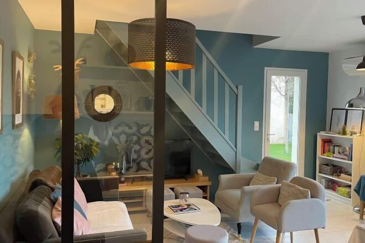 A modern living room with a sofa, armchairs, a coffee table, a fireplace, and a staircase.