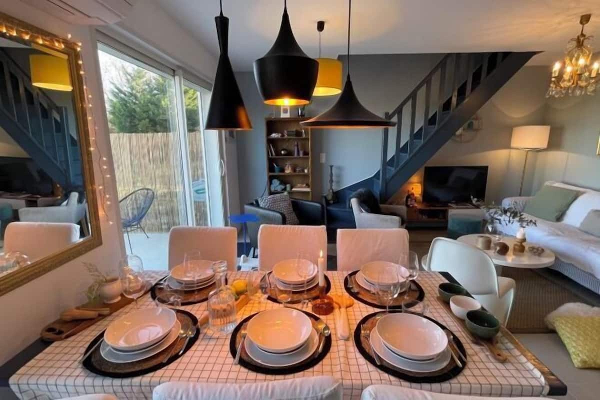 A dining area with a table set for six, a staircase, and a living room with a sofa and a TV.