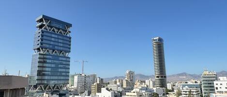 Un paisaje urbano con edificios modernos, incluyendo un rascacielos distintivo con un diseño en zigzag y una torre cilíndrica.