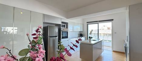 Cocina moderna con refrigerador, microondas y horno. Cuenta con un comedor con mesa y sillas, y un amplio ventanal con vista a la ciudad.