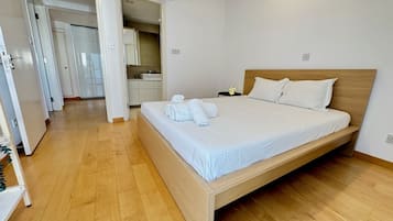 Ett modernt hotellrum med en säng i trä, vita sängkläder och ett badrum med synliga detaljer, inklusive handfat och spegel.