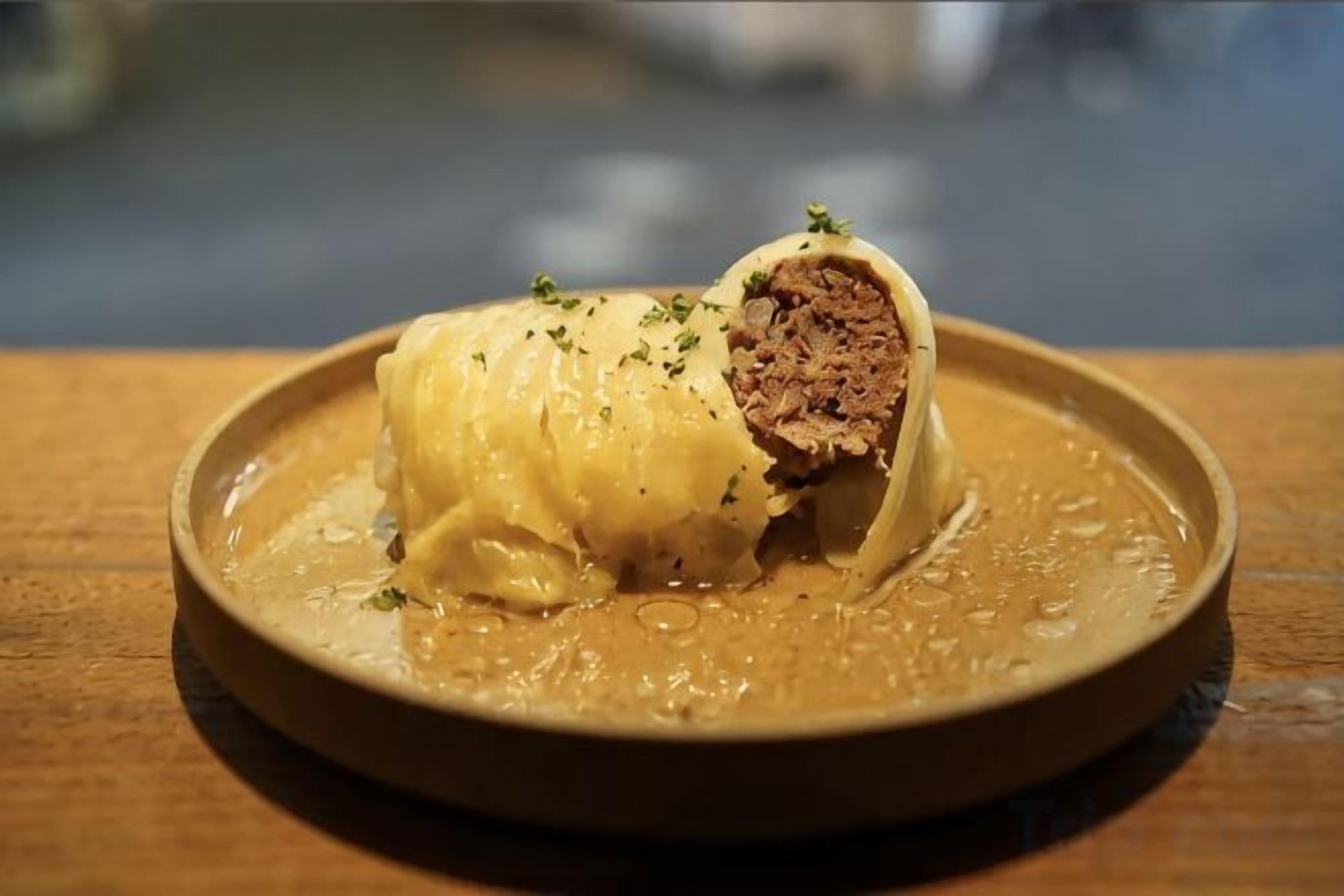 Un plato con un alimento enrollado, posiblemente un pastel relleno de carne, adornado con hierbas.
