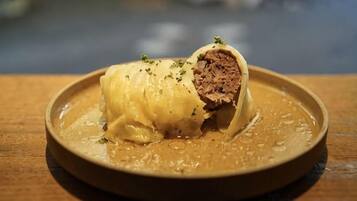 Un plato con un alimento enrollado, posiblemente un pastel relleno de carne, adornado con hierbas.