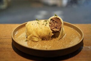 Un plato con un alimento enrollado, posiblemente un pastel relleno de carne, adornado con hierbas.