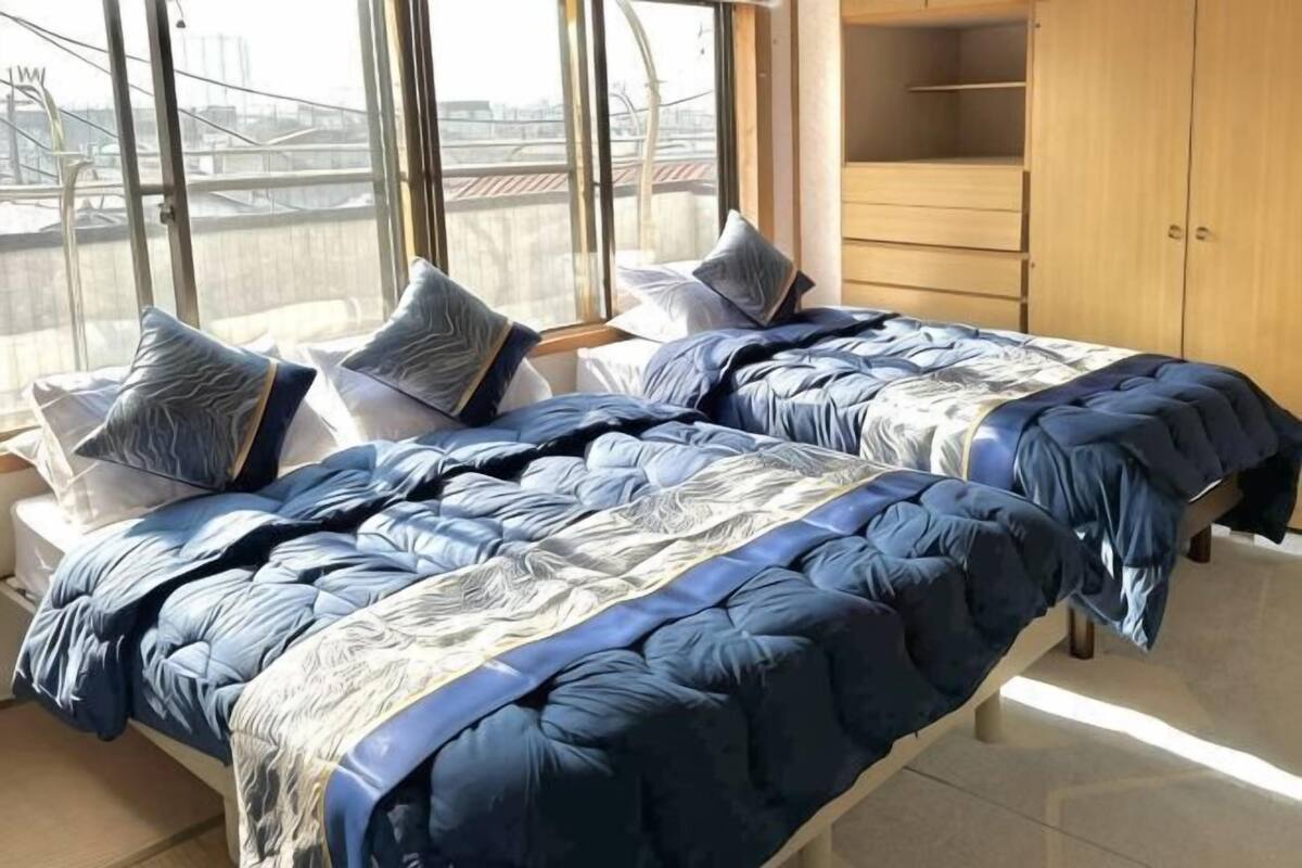 Zwei Betten mit blauer Bettwäsche, ein Holzschrank und der Blick auf eine Brücke durch große Fenster.