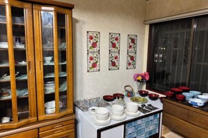 Una cocina con un armario de madera, una mesa con vajilla y un ventanal con persianas.
