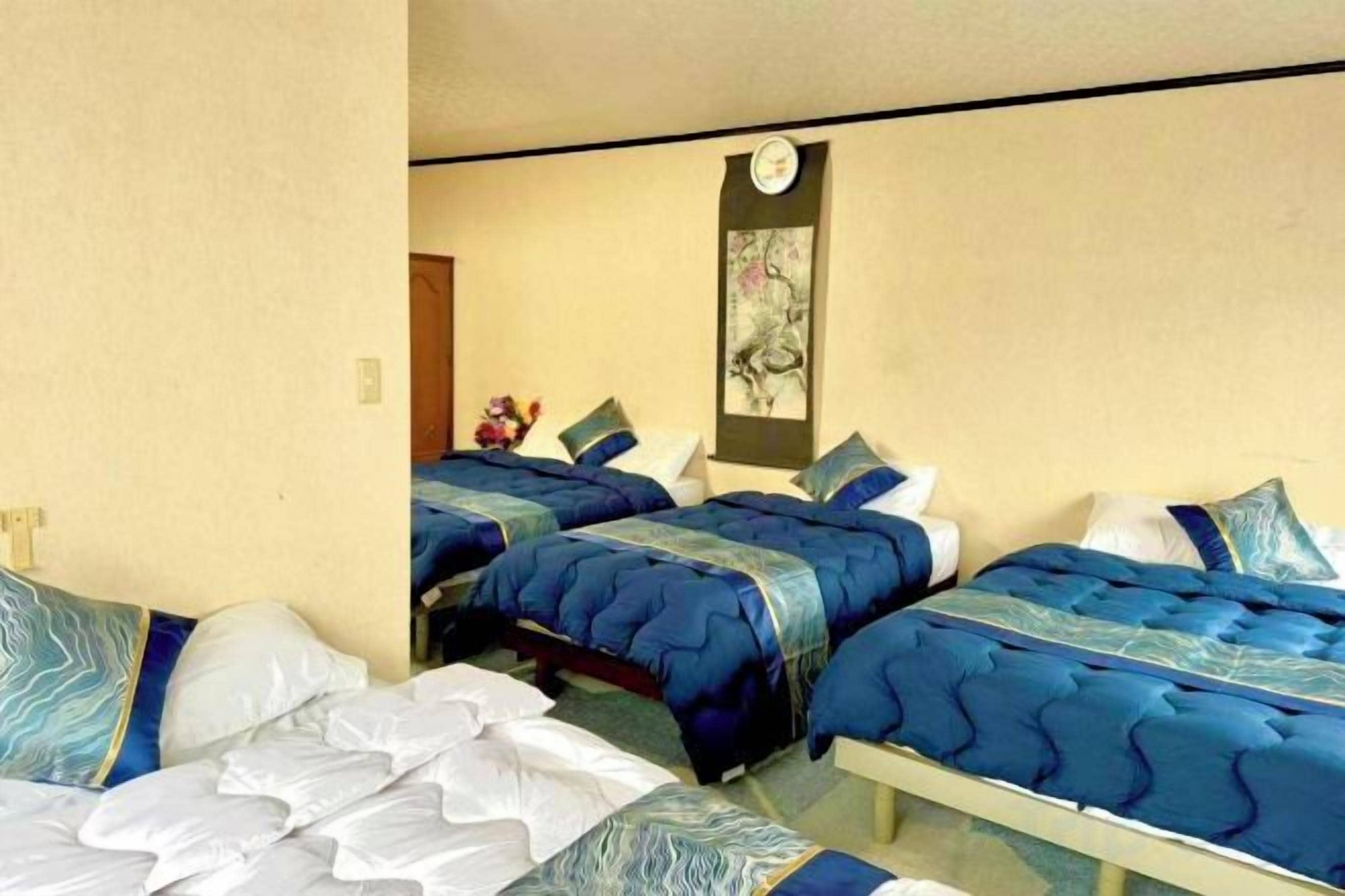 A hotel room with two beds, a small table, and a wall-mounted clock.
