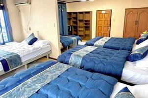 Habitación de hotel con cuatro camas dispuestas en fila, un armario de madera y una ventana con cortinas.