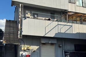 A multi-story building with a closed garage door, external electrical boxes, and a visible balcony. - Mito Houses 19-23 Pax - Breakfast Options (Higashiosaka)