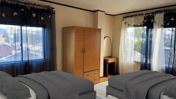 A bedroom with two beds, a wardrobe, a desk, and a window with curtains.