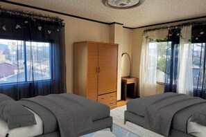 A bedroom with two beds, a wardrobe, a desk, and a window with curtains. - Mito Houses 19-23 Pax - Breakfast Options (Higashiosaka)