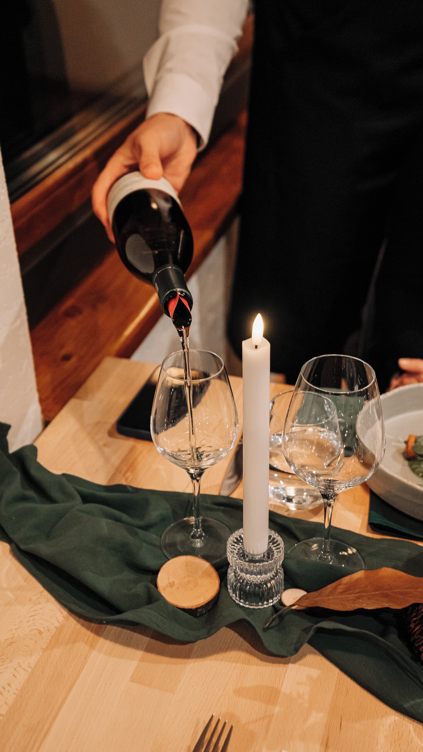 A candle on a table with glasses and a bottle of water.