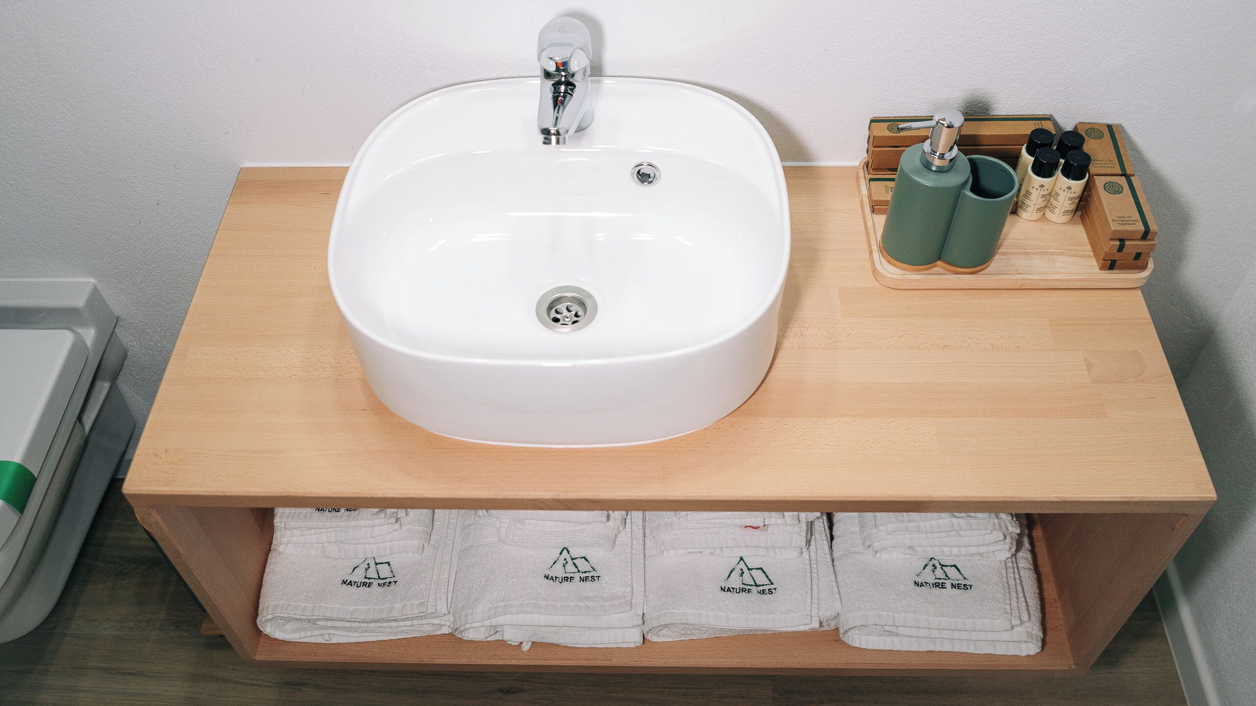 Un baño con lavamanos blanco, tocador de madera y toallas dobladas con un logotipo.