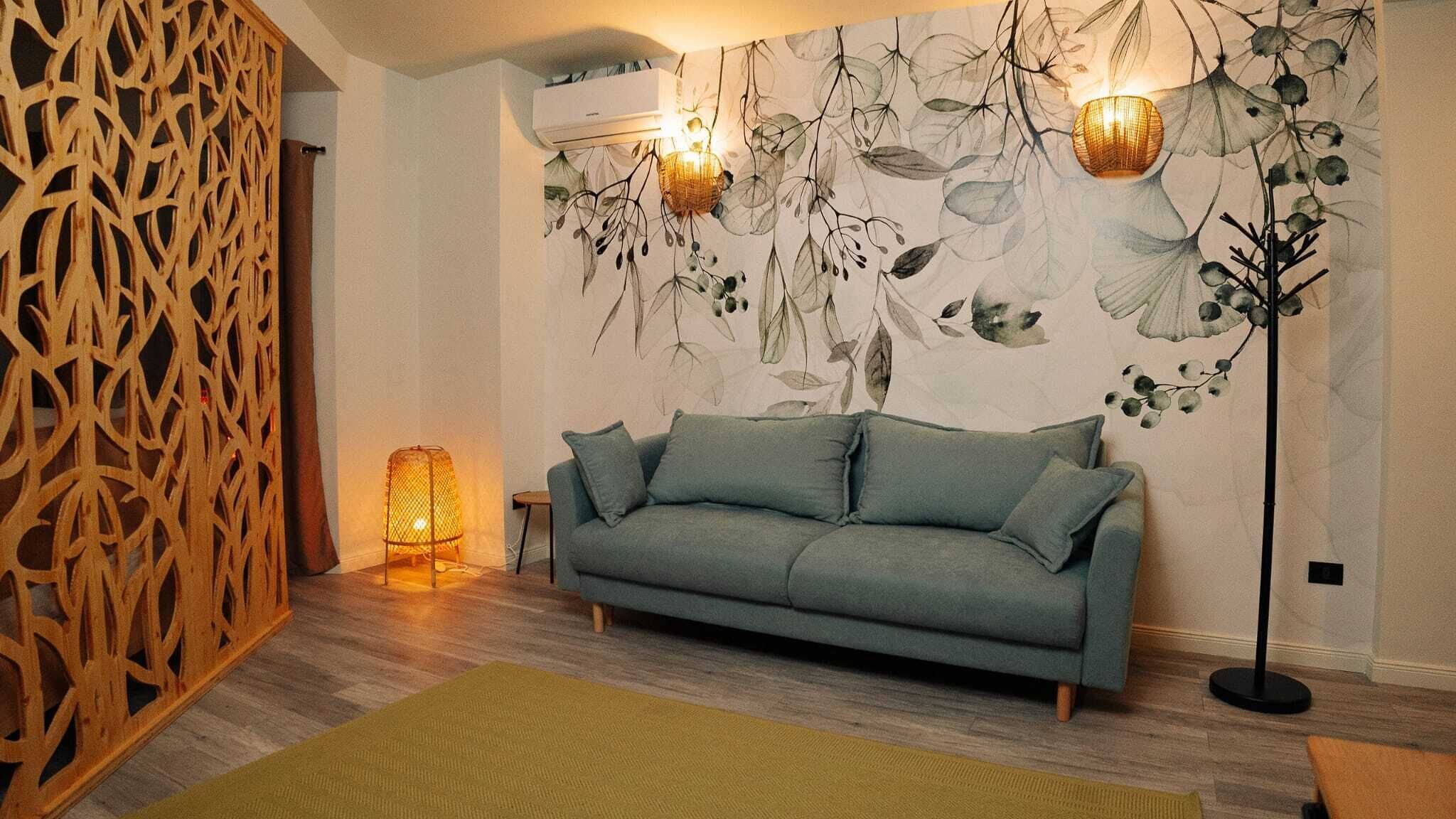Un soggiorno moderno con un divano grigio, una parete decorata con motivi a foglia, una lampada da terra e un pannello in legno.