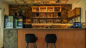 A bar area with a wooden counter, two black bar stools, and shelves with bottles and glasses. - Nature Nest (Bran)