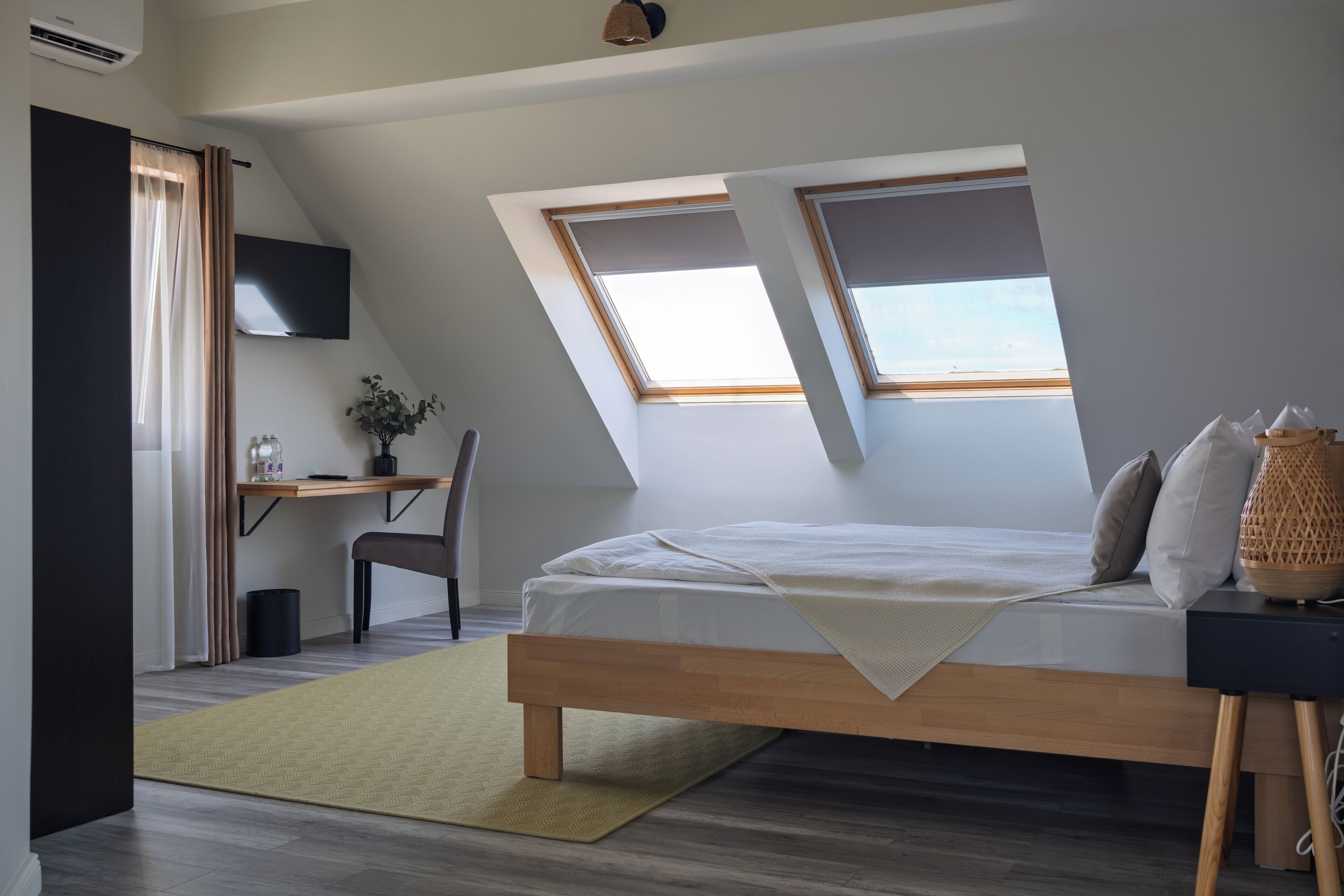 Un dormitorio moderno con techo inclinado, ventanas de tragaluces, cama, escritorio y silla.