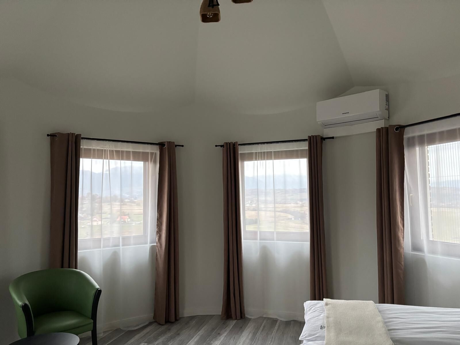 A hotel room with a bed, a chair, and two windows with curtains.