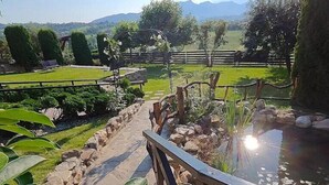A garden pathway leading to a pond with a wooden fence and a view of distant mountains. - Nature Nest (Bran)