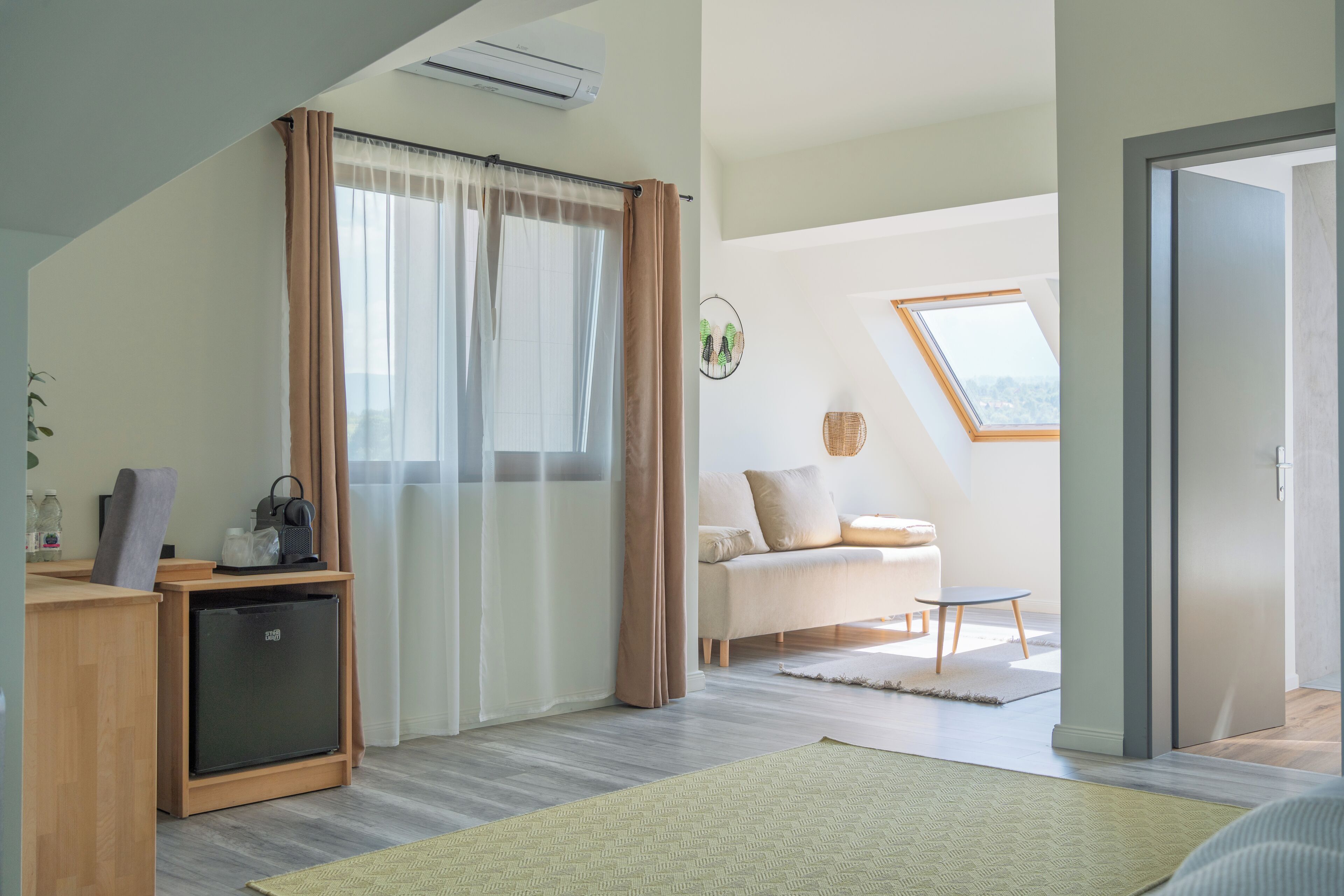Quarto moderno com cozinha compacta, sofá, mesa pequena e janela com cortinas.