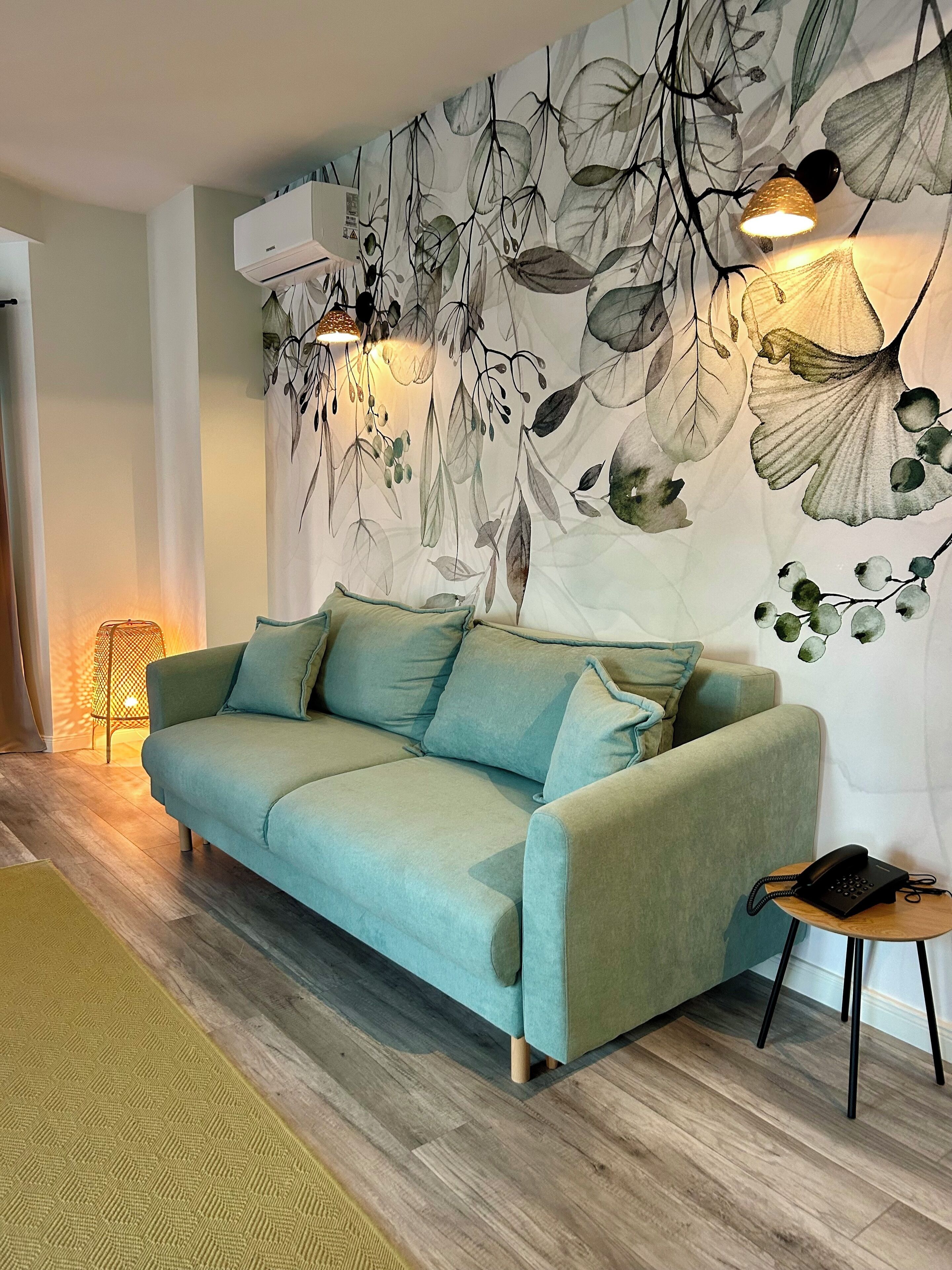 Una sala de estar moderna con un sofá verde claro, un mural con diseño, una mesita auxiliar con un teléfono y una lámpara de pie.