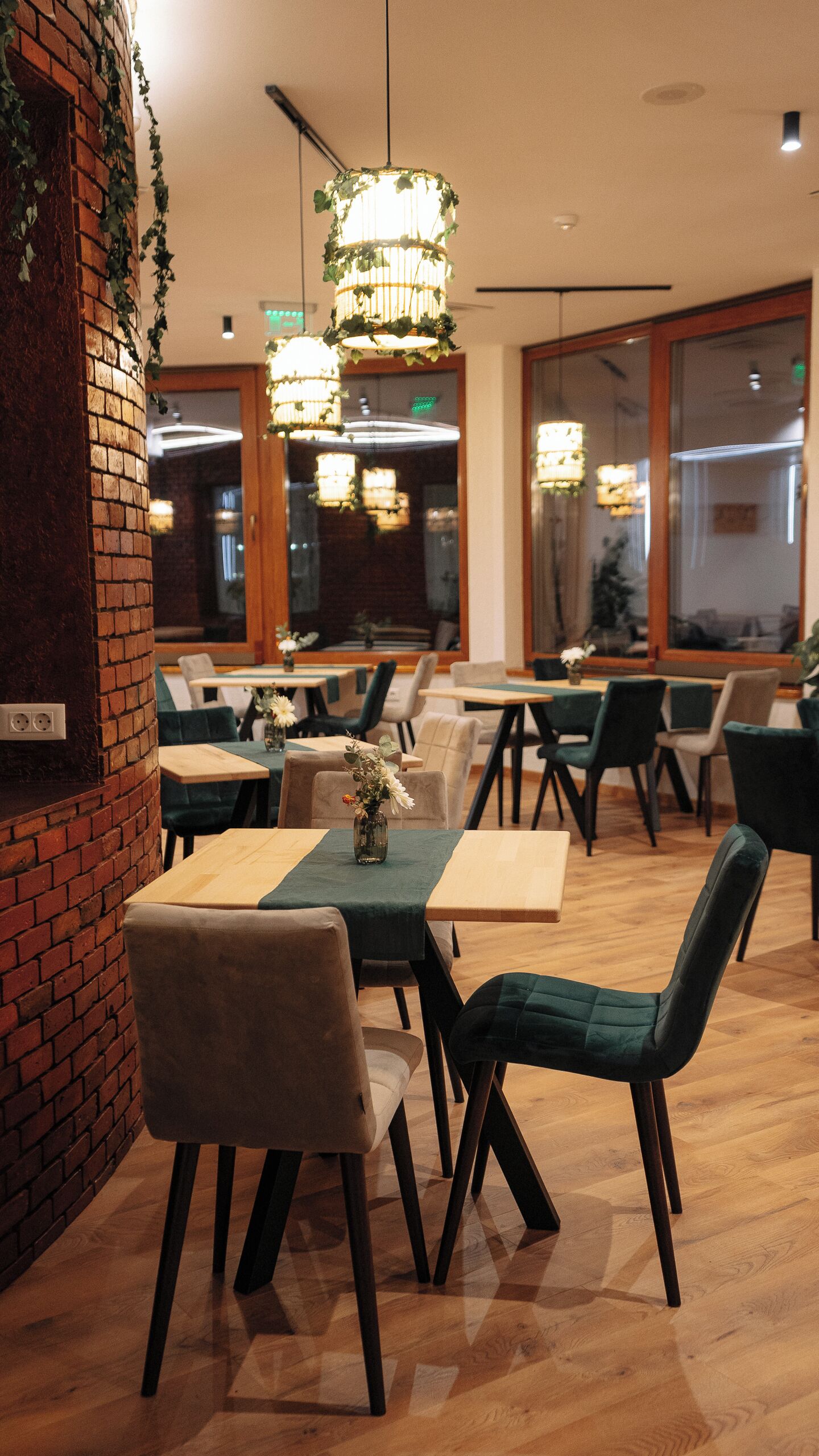 A restaurant interior with brick walls, wooden tables, and green upholstered chairs.