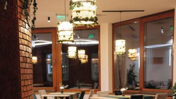 A restaurant interior with brick walls, wooden tables, and green upholstered chairs.
