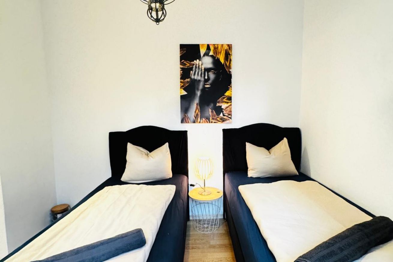 Une chambre avec deux lits, une œuvre d’art accrochée au mur et une petite table avec une lampe.