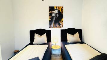 Une chambre avec deux lits, une œuvre d’art accrochée au mur et une petite table avec une lampe.