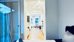 Un dormitorio con una cama, una ventana y vistas a un pasillo que lleva a una cocina.