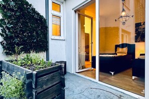 A room with a bed, a chair, a wooden planter with plants, and a sliding glass door leading to another room. - Lovely 2BR for 5 | Peaceful & Central Stay (Klosterneuburg)
