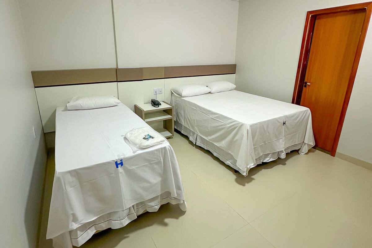 A hotel room with two single beds, a wooden door, and a small bedside table with a phone.