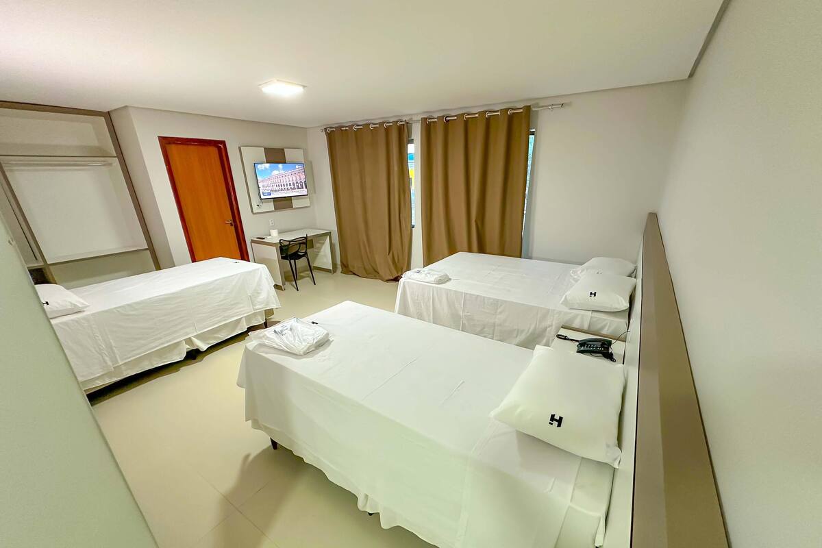 A hotel room with two single beds, a desk, a chair, a TV, and a window with curtains.