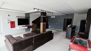 A modern living room with a sectional sofa, a flat-screen TV mounted on the wall, and a staircase leading to another level. - Hotel Ideal 5  (Araguaína)