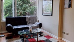 Ein Wohnzimmer mit einer schwarzen Couch, einem Glastisch und einem karierten Teppich.