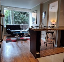 Una cocina moderna con barra, una mesa de comedor y un sofá en una sala de estar con ventanas amplias.