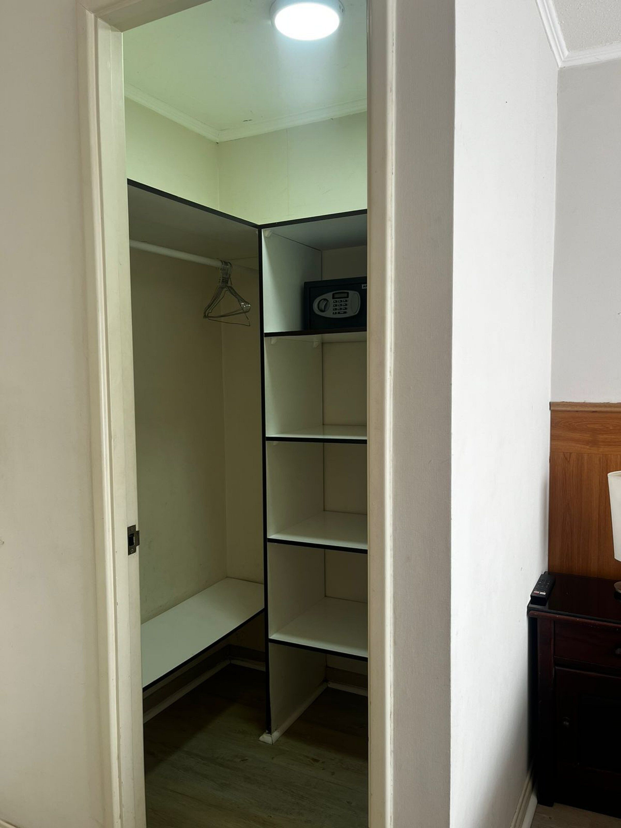 A walk-in closet with a hanging rack and a microwave on the shelves.