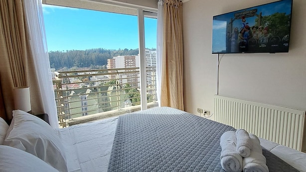 Ein Hotelzimmer mit einem großen Bett, einem an der Wand befestigten Fernseher und einem Fenster mit Vorhängen.