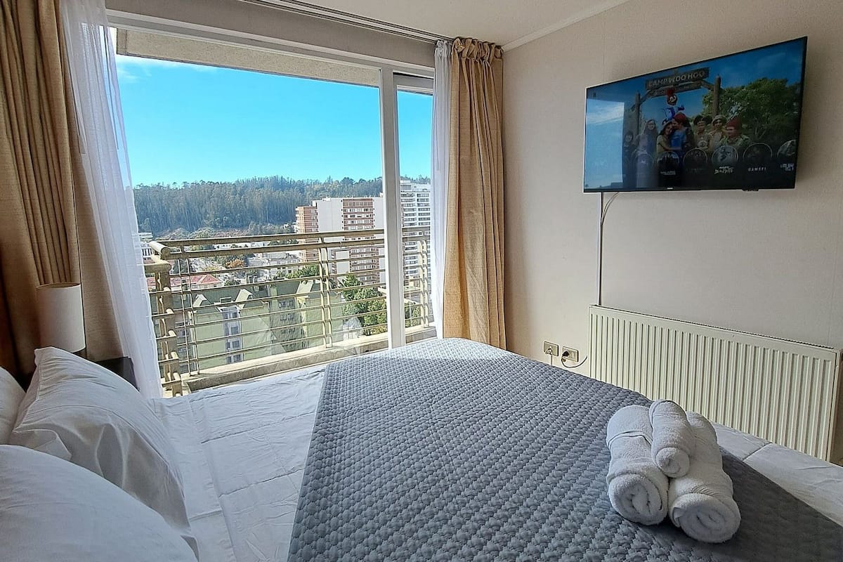 Camera d'albergo con un letto grande, una TV fissata al muro e una finestra con tende.