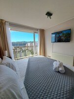 Habitación de hotel con una cama grande, un televisor montado en la pared y una ventana con cortinas.