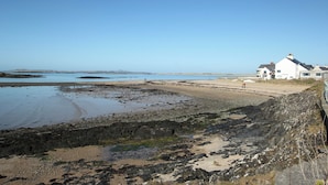 A coastal scene with a white building, rocky shoreline, and calm sea. - The Swell by Guestz (Rhosneigr)