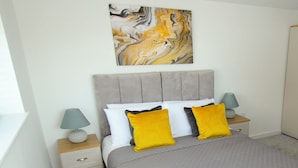 A bedroom with a grey upholstered bed, two bedside tables with lamps, a radiator, and a marble artwork on the wall. - The Swell by Guestz (Rhosneigr)